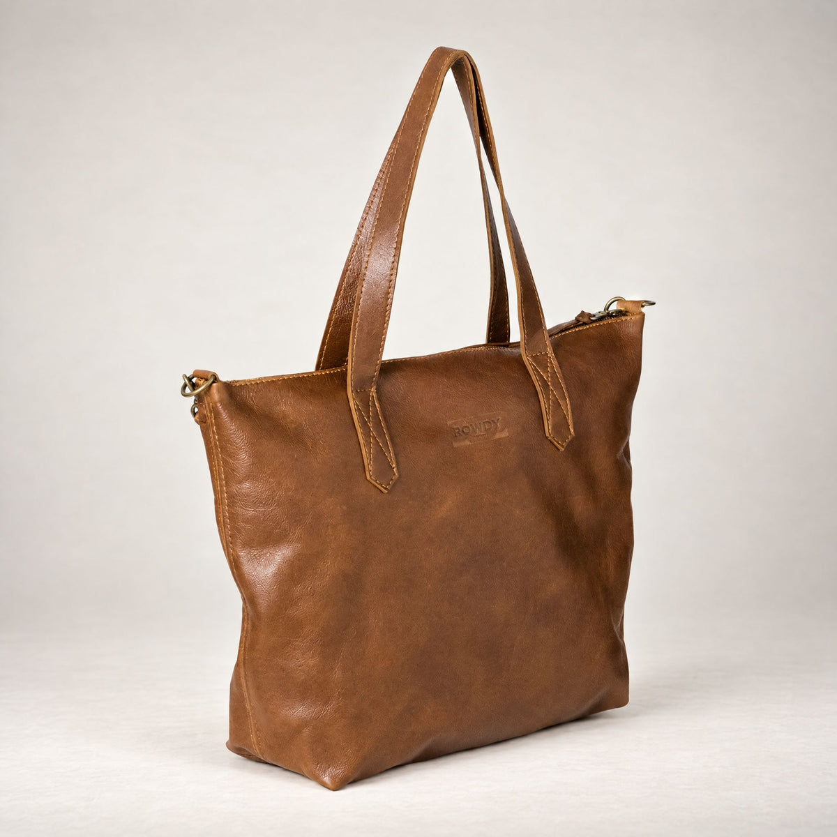 Rowdy Leather Crossbody Bag in Cedar (smooth aniline leather), three-quarter view showing the zip top and grab handles