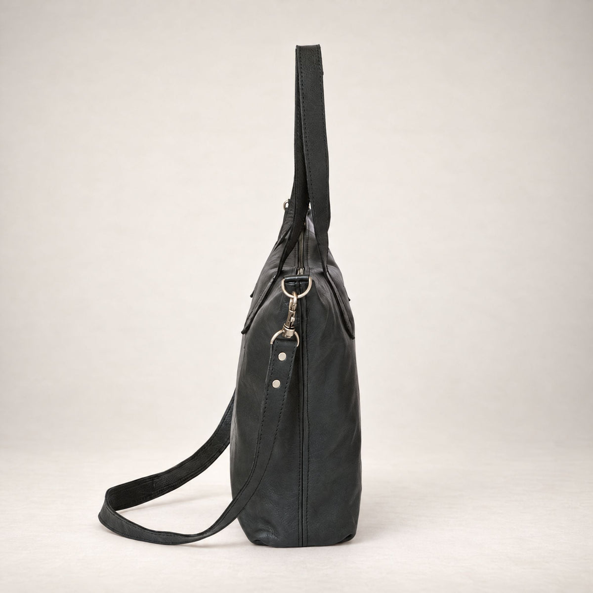 Rowdy Leather Crossbody Bag in Charcoal (black leather), three-quarter view showing the zip top and grab handles
