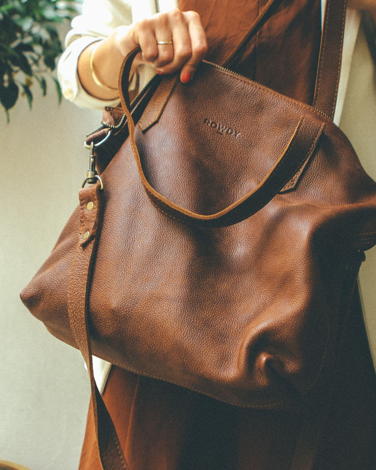 Rowdy Leather Crossbody Bag in mountain nubuck leather, held by its short handles with the shoulder strap clipped on