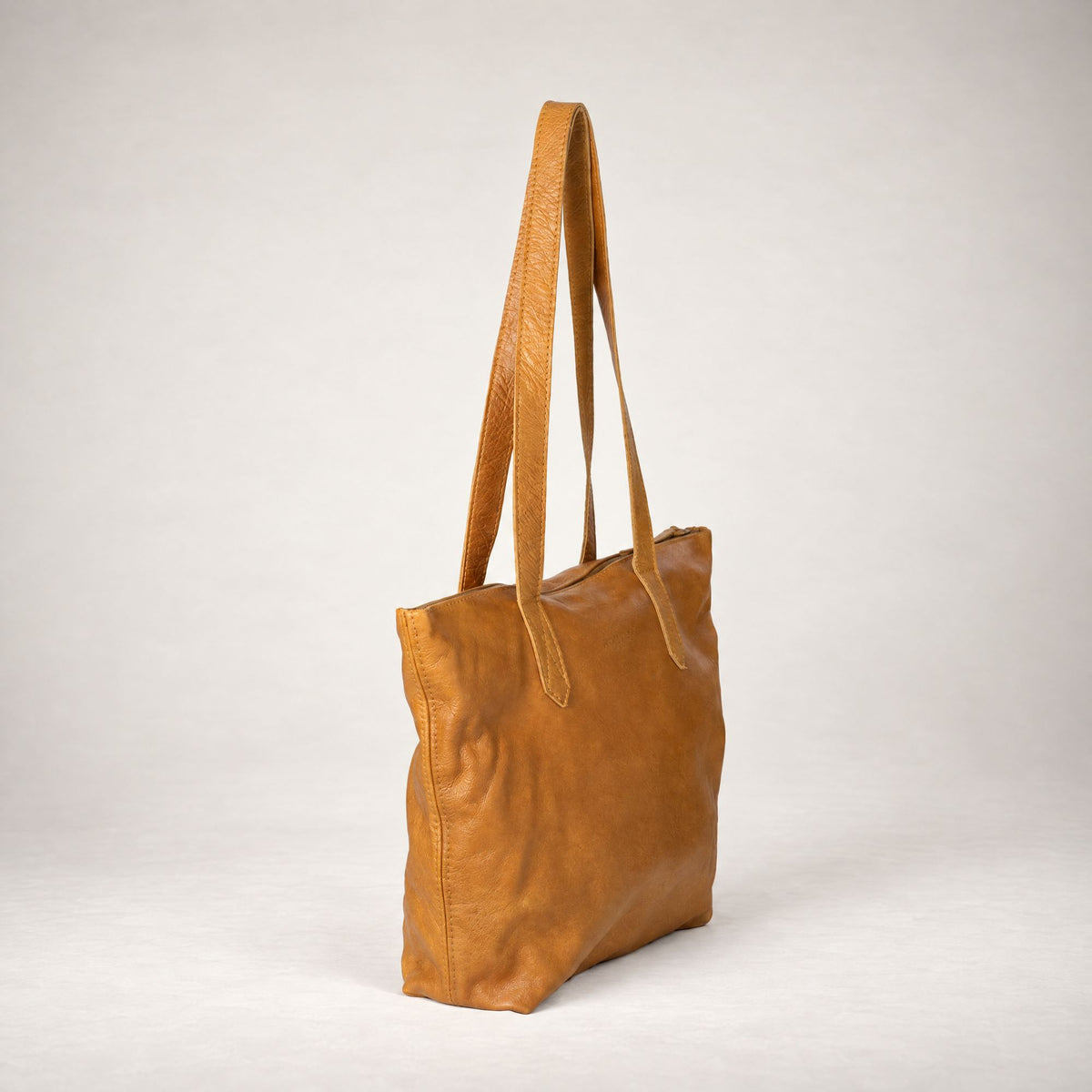 Rowdy Leather Tote Bag in Amber (smooth aniline leather), three-quarter view showing the zip top and long shoulder straps