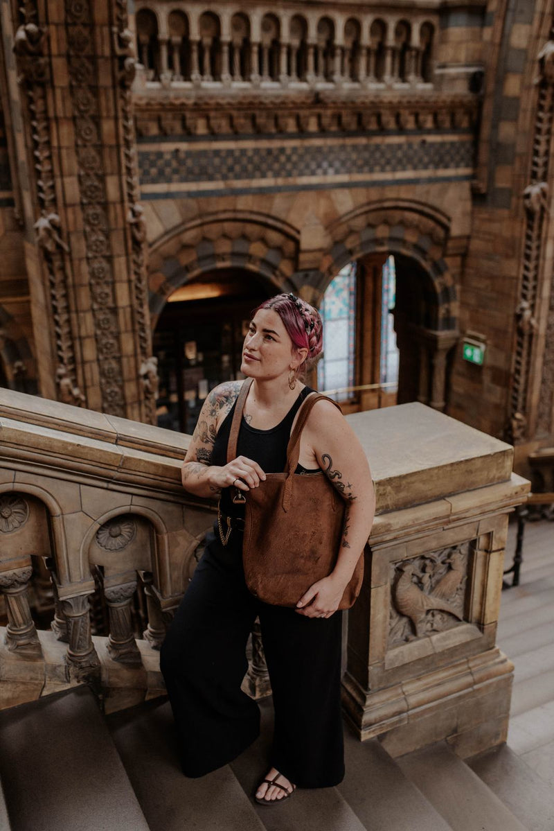 Woman in a black vest and wide black trousers with the Rowdy Leather Crossbody Bag on her shoulder on stone stairs
