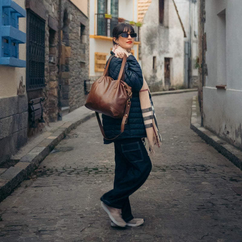 Woman on a cobbled street wearing a navy puffer gilet and check scarf, with the Rowdy Leather Crossbody Bag on her shoulder