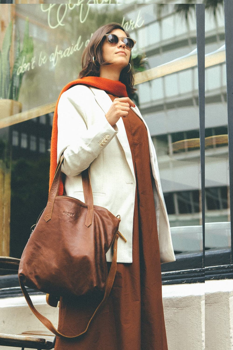 Woman in a cream blazer, orange scarf and rust dress carrying the Rowdy Leather Crossbody Bag on her arm