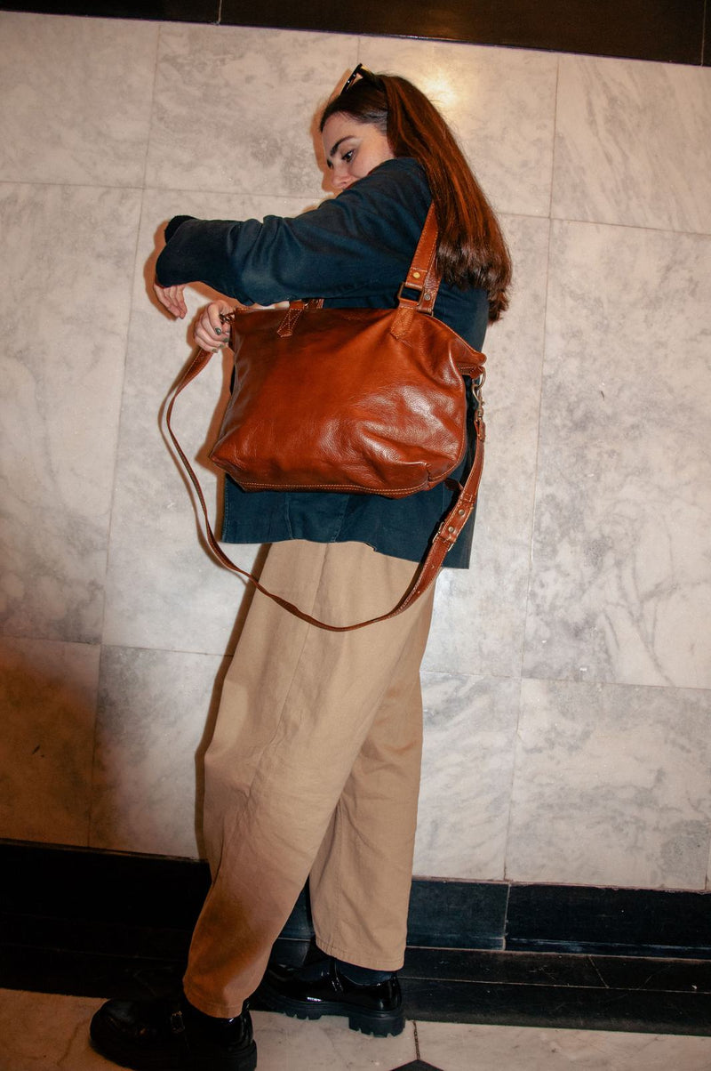 Woman in a navy jacket and camel wide-leg trousers adjusting the strap of the Rowdy Leather Crossbody Bag