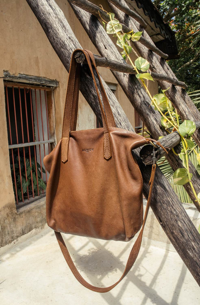 Rowdy Leather Crossbody Bag in Mountain hanging from a rustic wooden ladder in the sun