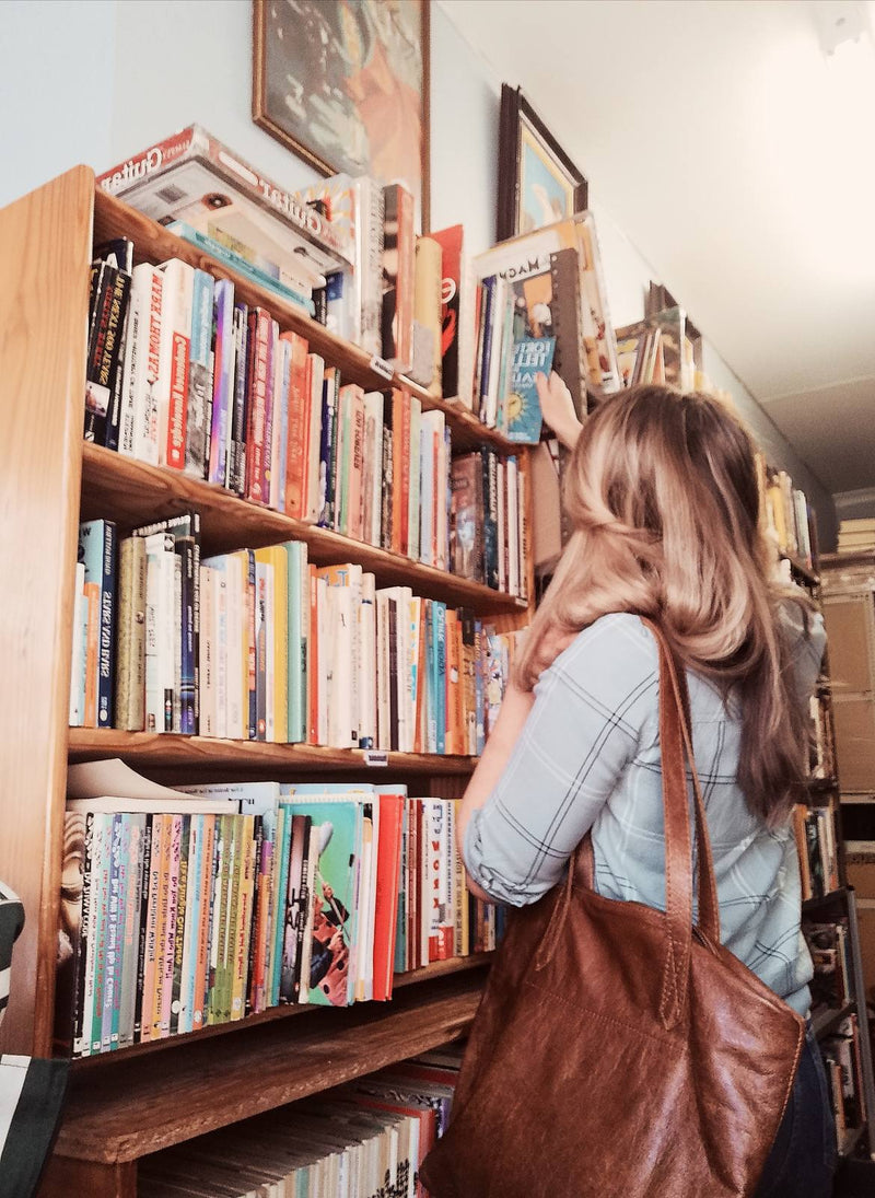 Woman browsing a bookshop with a tan Rowdy Leather Tote Bag on her shoulder