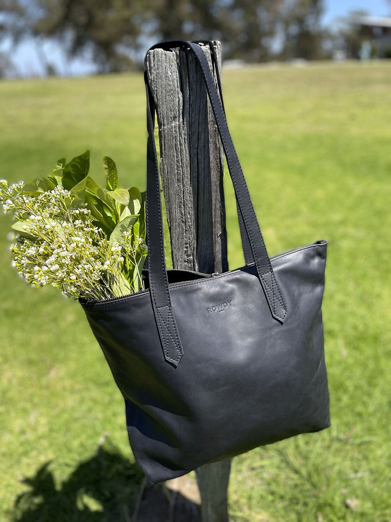 Black Rowdy Leather Tote Bag with flowers, hung on a fence post