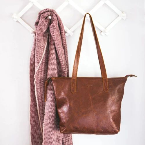 Tan Rowdy Leather Tote Bag hanging from a peg rail beside a herringbone wool scarf