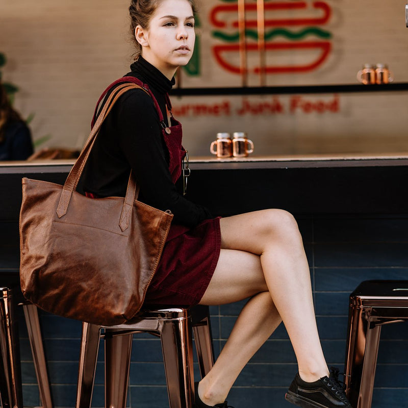 Woman seated at a café counter wearing the Rowdy Leather Tote Bag on her shoulder