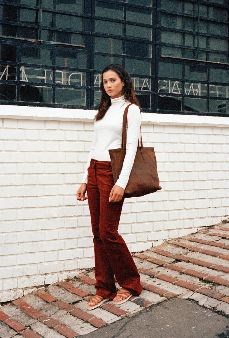 Woman in a white roll neck and rust cord flares with a brown Rowdy Leather Tote Bag on her shoulder